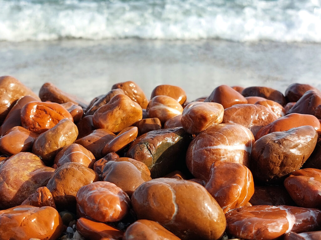Stones of jasper sit on a water's shore.