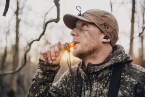 A hunter wear the first lite-stormy kromer cap while using an animal call in the woods.