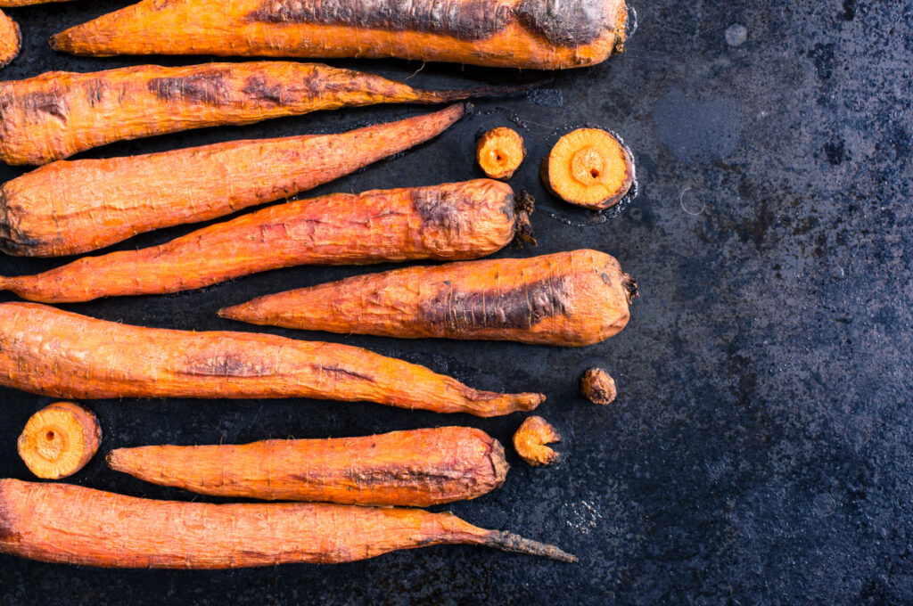 Several roasted carrots on a blacktop grill