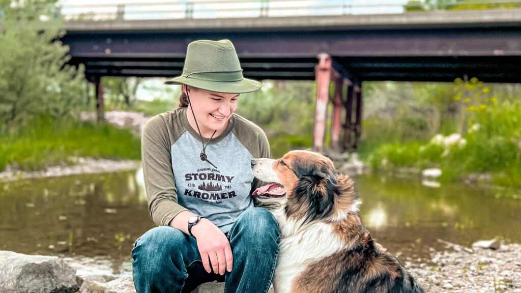 KC Spring Launch Blog THe Mesh Hiker @melodymaephotography Melody hiking with their dog and sitting next to a river petting her dog