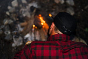 Hayden Dobbins sits by a campfire wearing a Stormy Kromer Cap