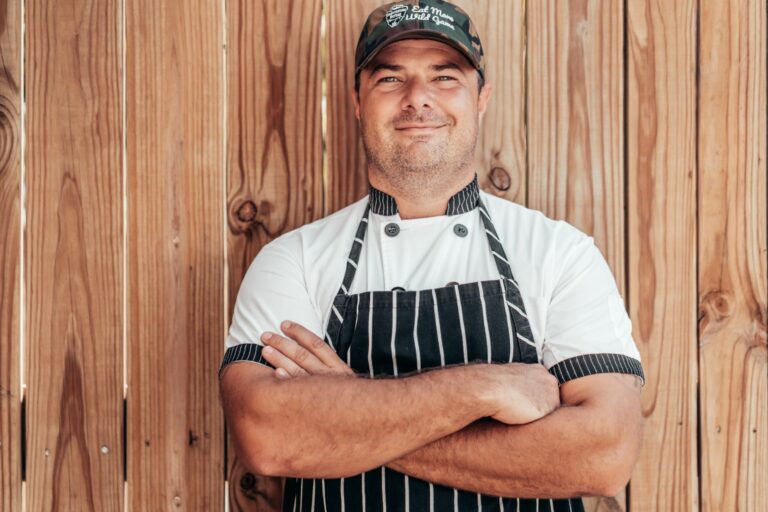 Justin Townsend of Harvesting Nature poses leaning against a wall in his chef's apron.