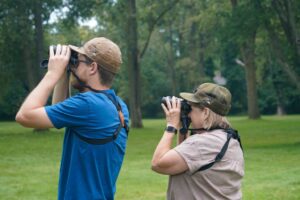 Two members of the Michigan Audubon look through binoculars while wearing their Michigan Audubon-Stormy Kromer Collaboration hats